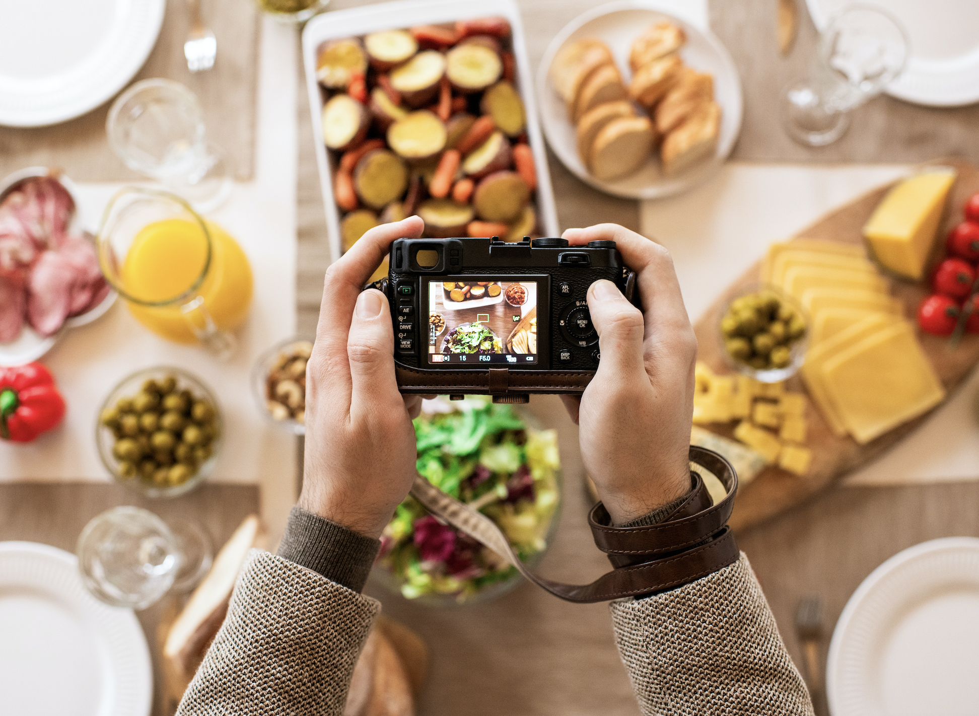 Someone holding a DSR camera with both hands, taking pictures of a table full of different foods.